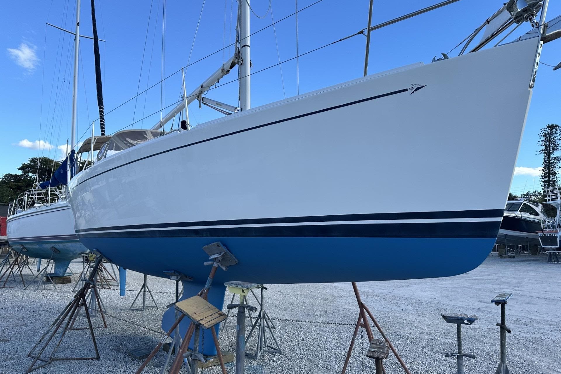 2004 J Boats J/32 sailboat on stands, white hull with blue stripe, clear sky background.