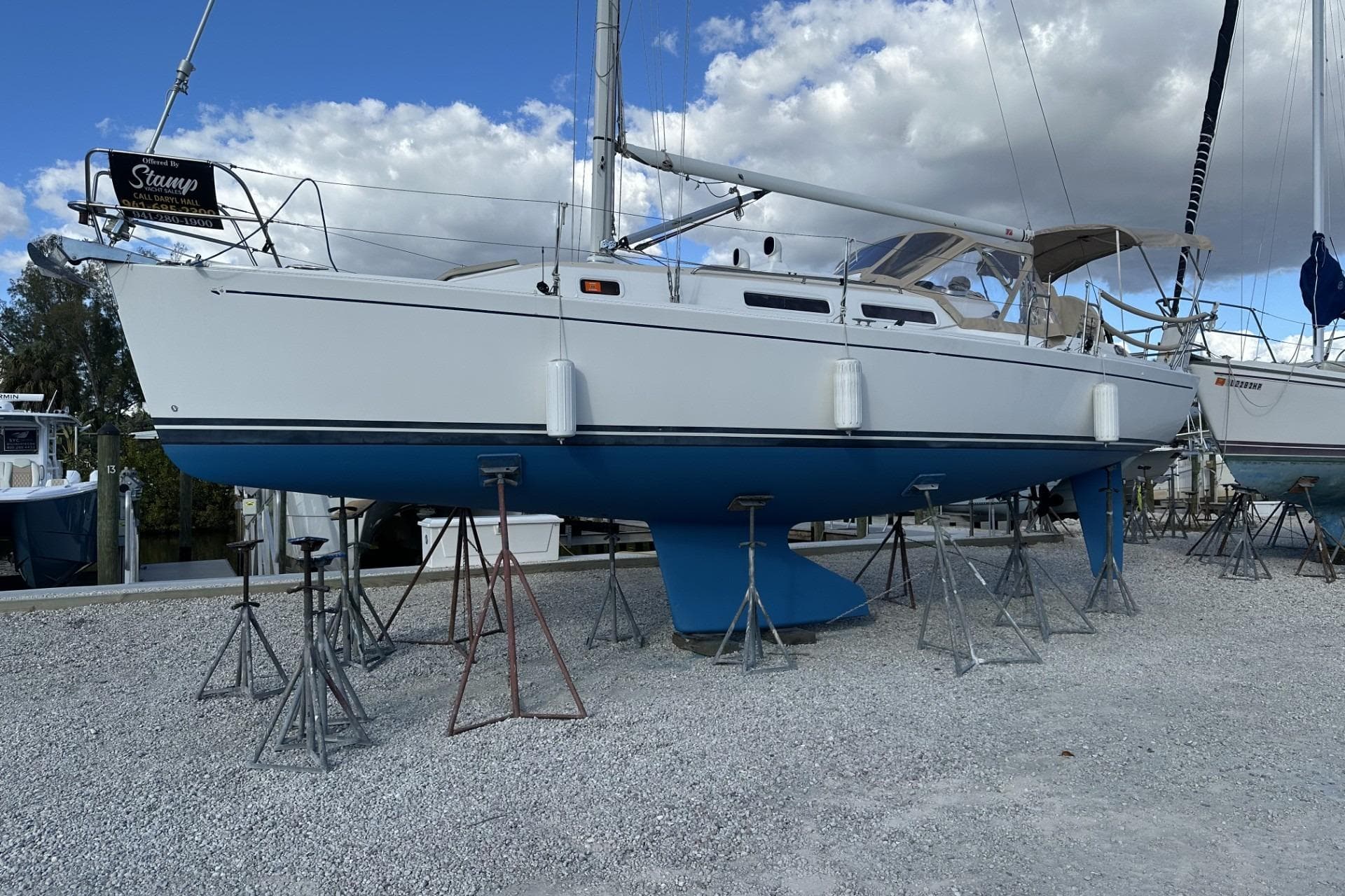 2004 J Boats J/32 sailboat on stands, white hull, blue bottom, cloudy sky background.