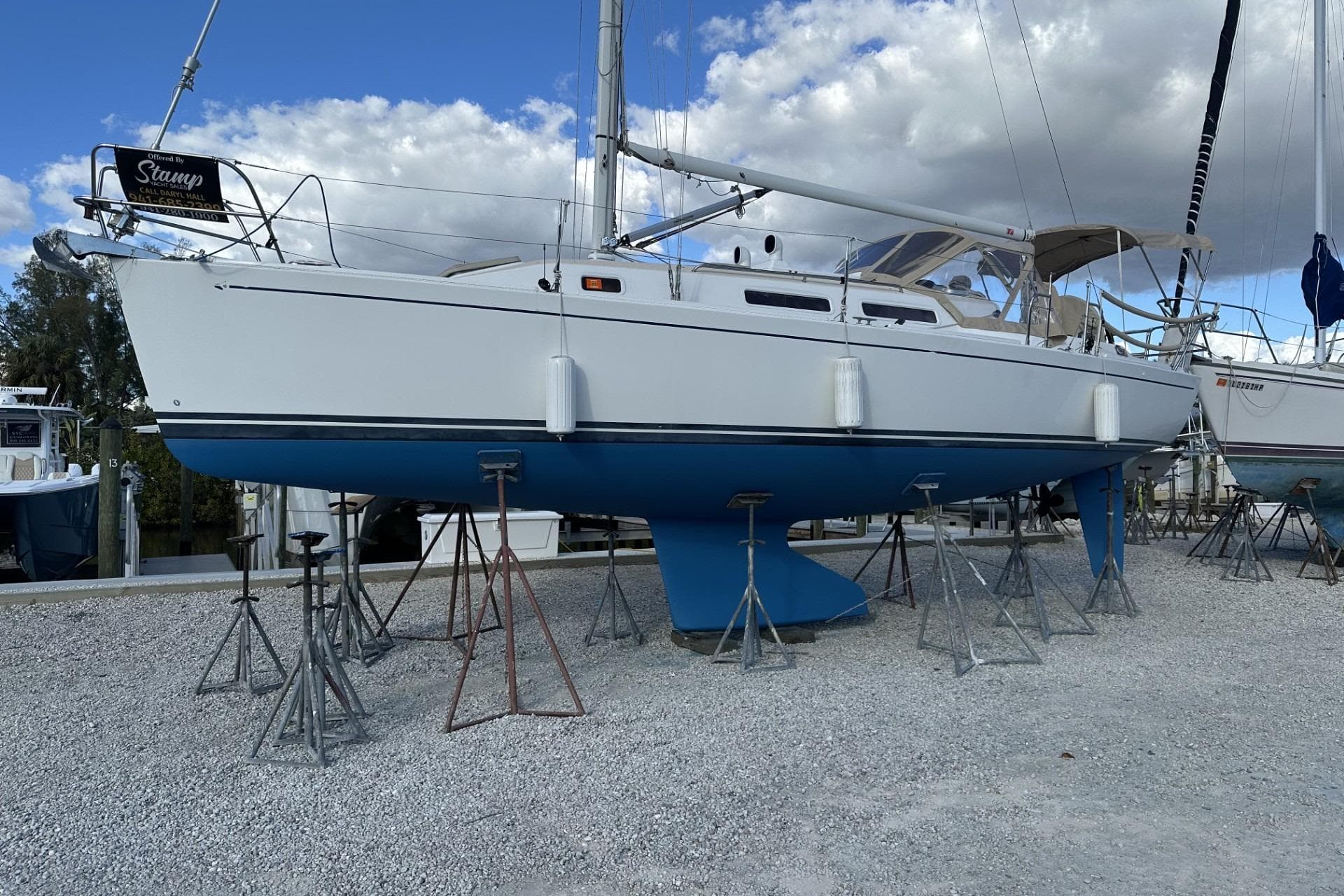 2004 J Boats J/32 sailboat on stands, white hull, blue keel, cloudy sky background.