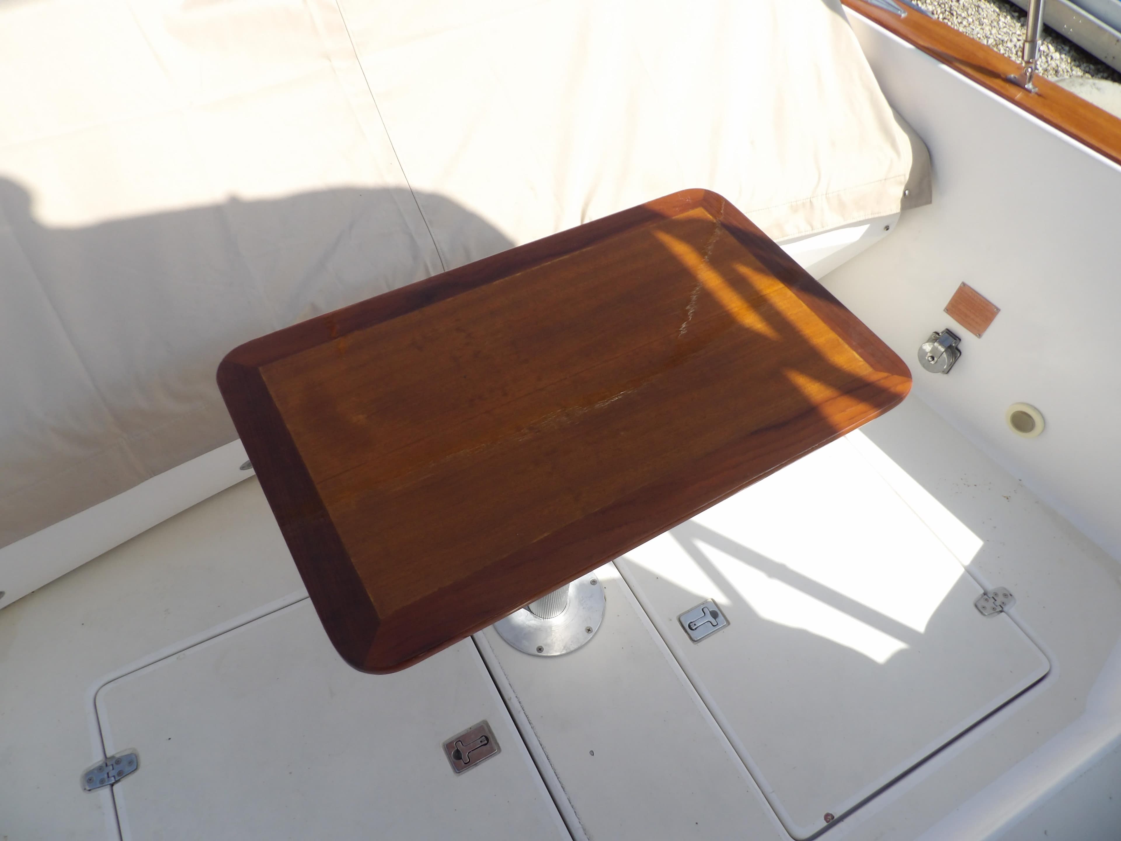 Wooden table on 2002 Legacy Yachts 28 Express deck, sunlight casting shadows.