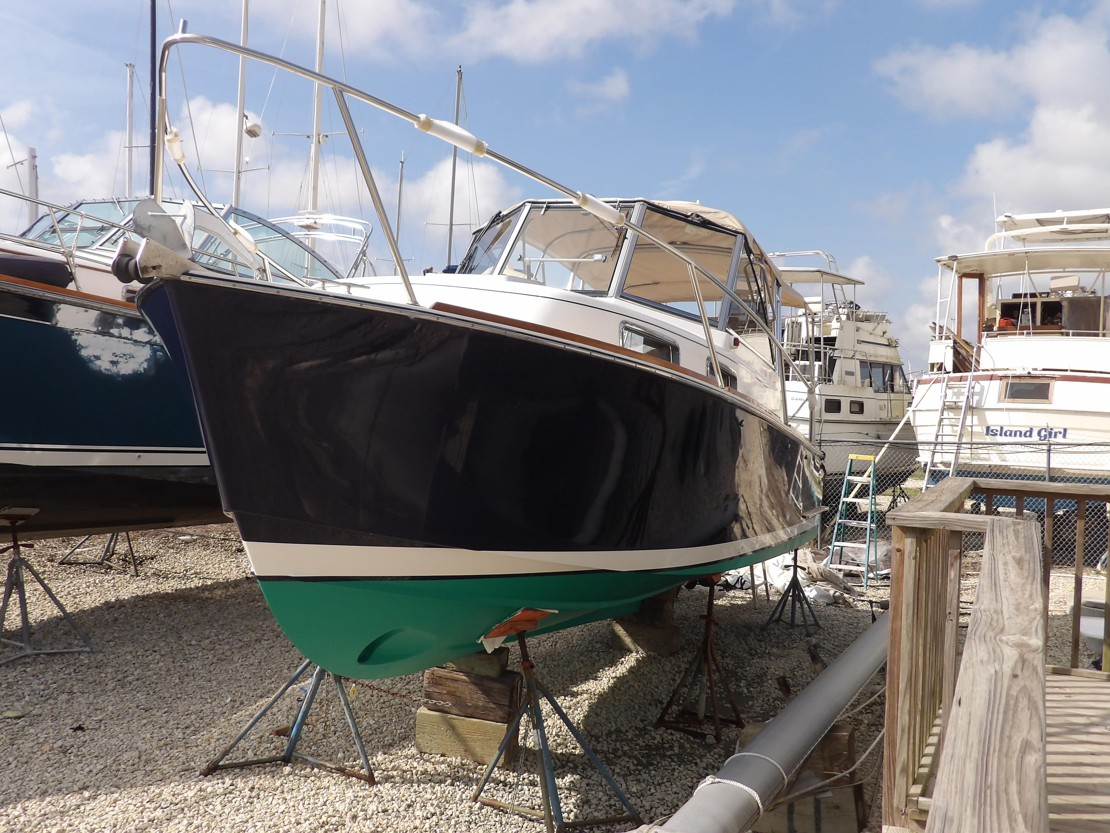 2002 Legacy Yachts 28 Express on dry dock, blue hull, green bottom, clear sky background.