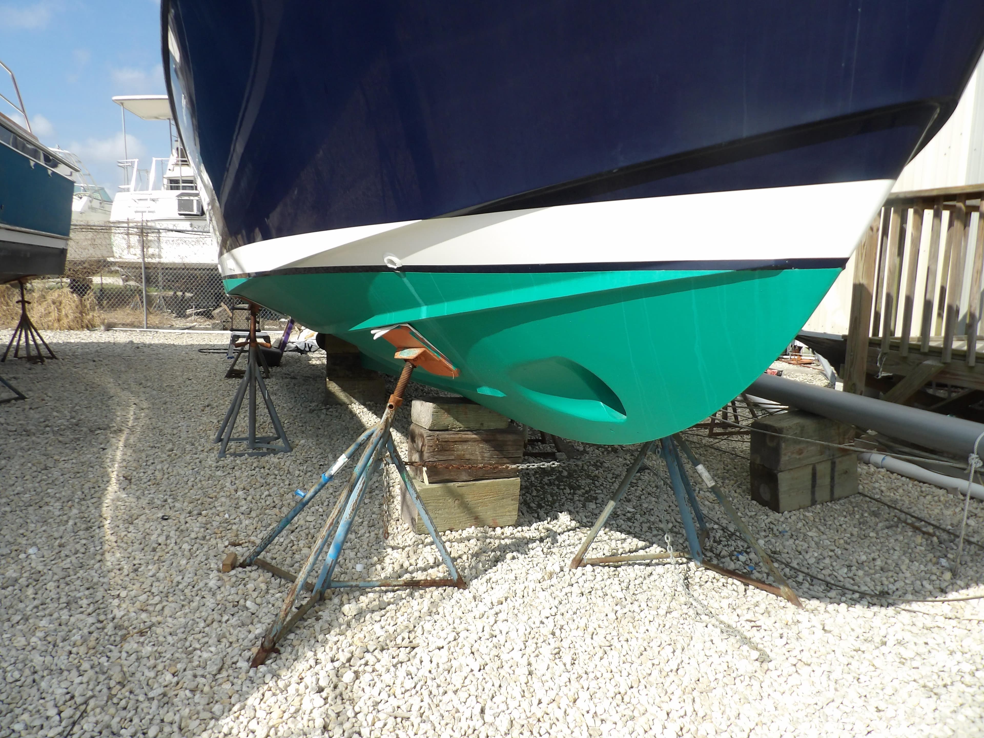 2002 Legacy Yachts 28 Express on stands, hull painted blue and green, resting on gravel.