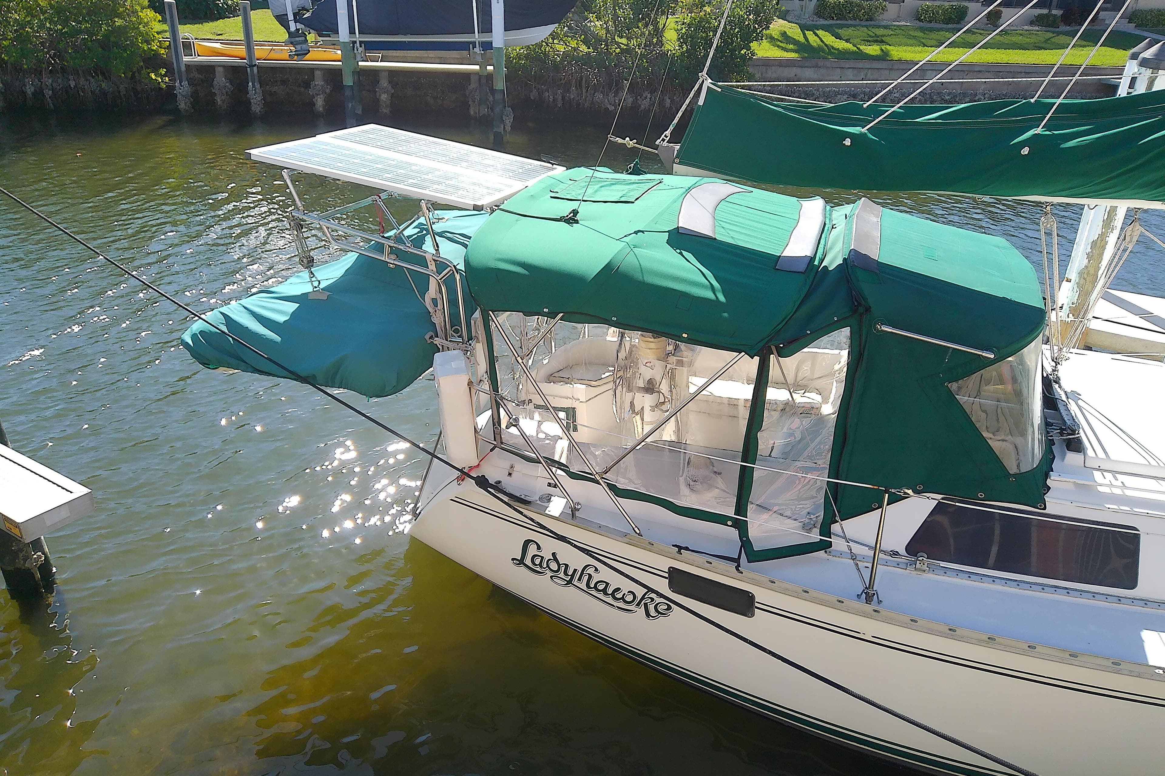 Hunter 30 sailboat from 1991 with green canopy docked in sunny marina.