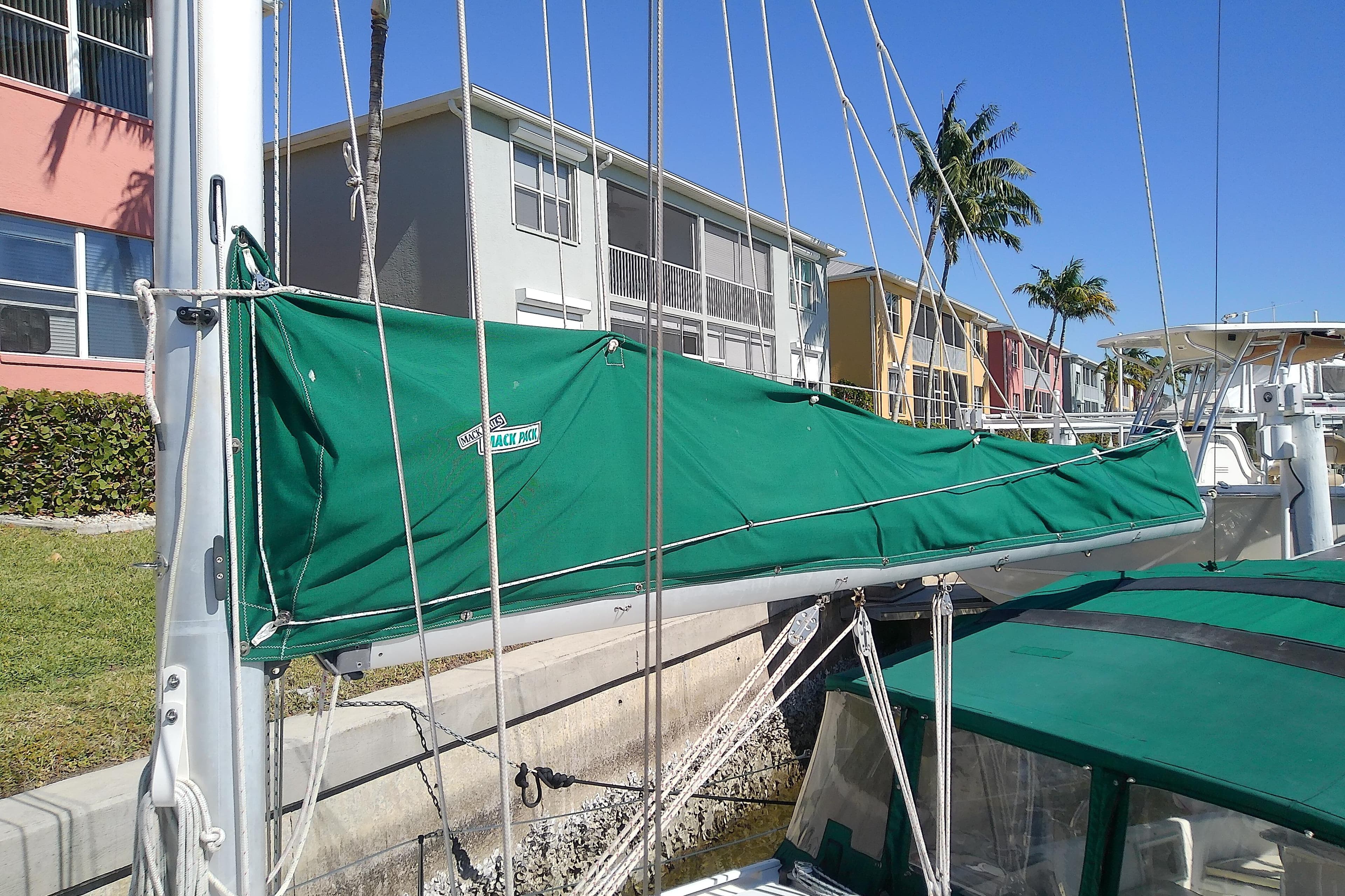 Hunter 30 sailboat from 1991 docked, featuring a green sail cover, with colorful buildings in the background.